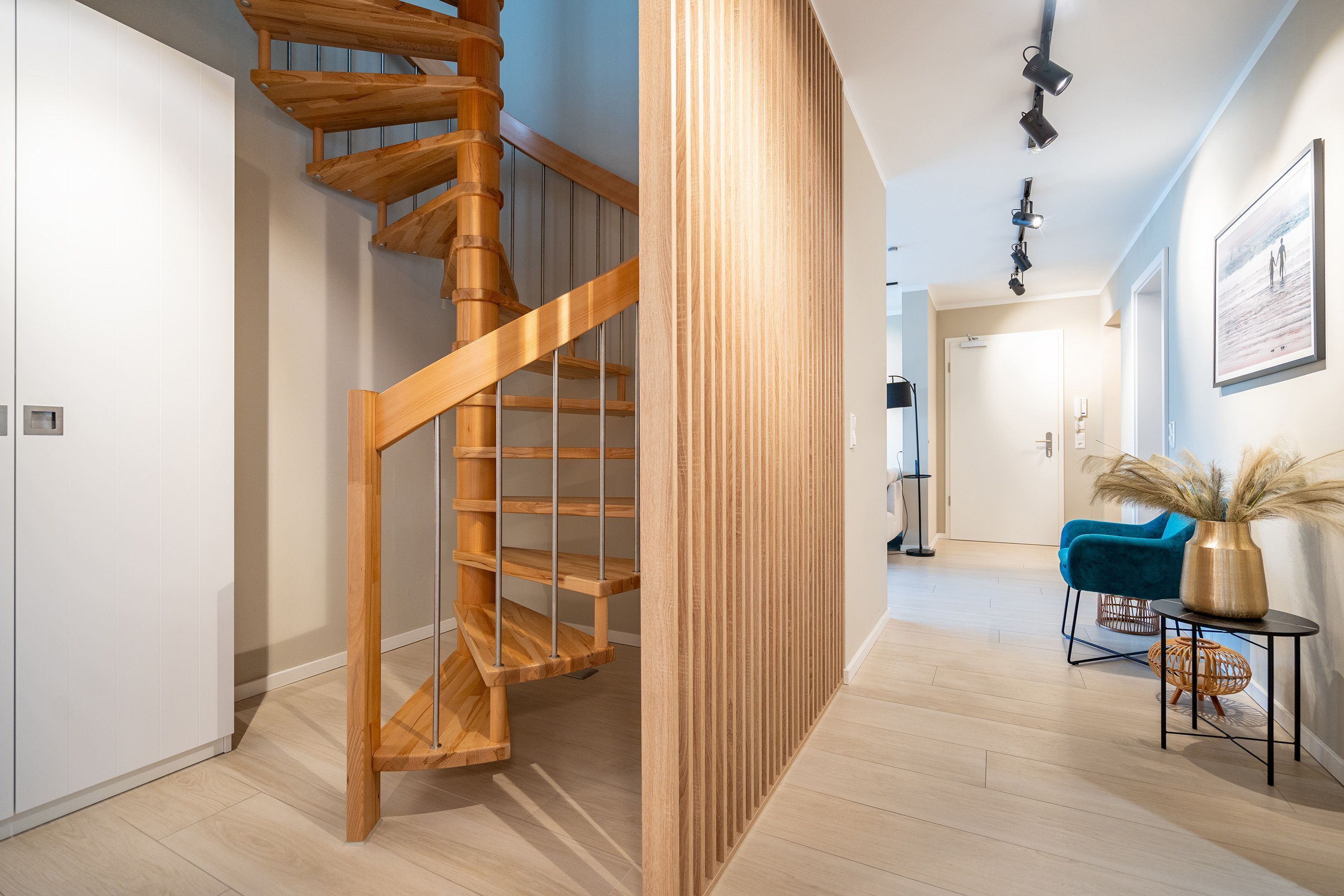 A modern interior with a wooden spiral staircase, a blue chair, and a vase with pampas grass.