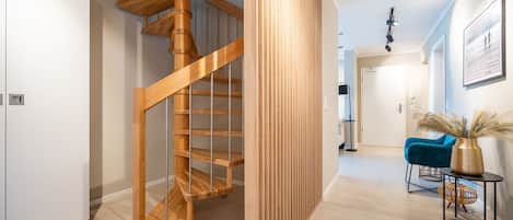 A modern interior with a wooden spiral staircase, a blue chair, and a vase with pampas grass.