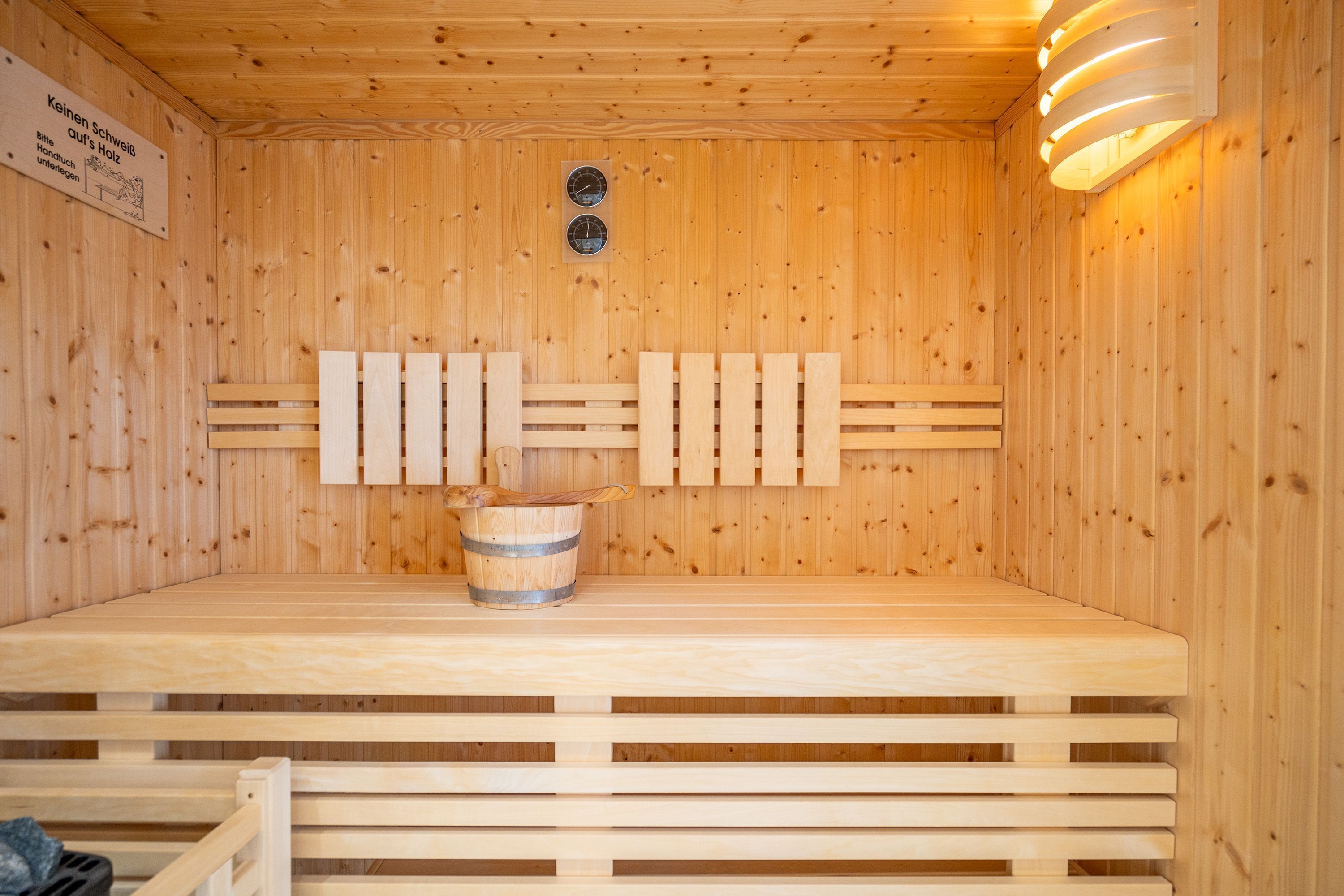 Eine Sauna mit Holzwänden und Bänken, ein Eimer und ein Schild mit Text.