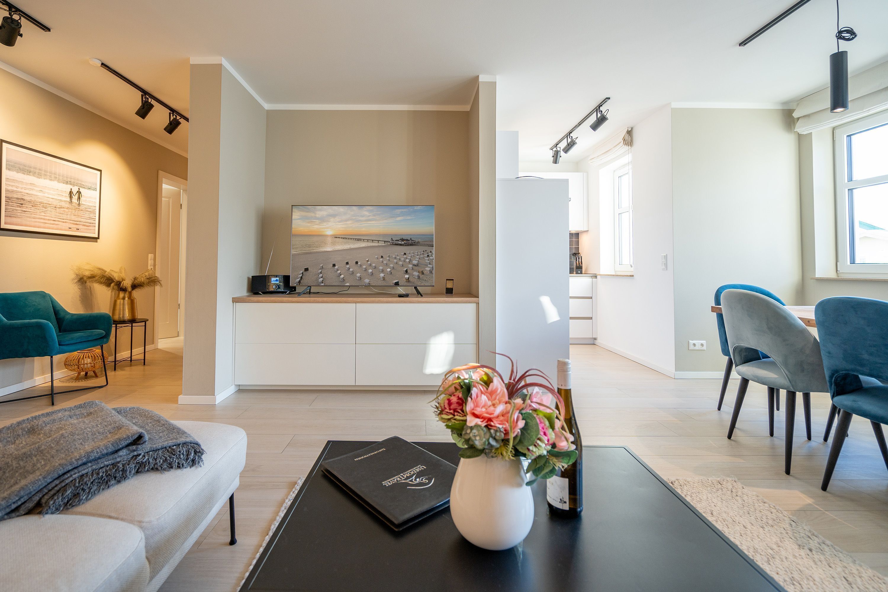 Una sala de estar moderna con un sofá, una mesa de centro con un florero, un área de comedor con sillas y una cocina al fondo.