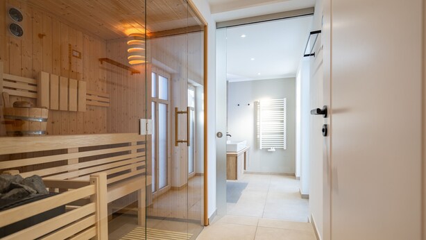 Una camera d'albergo moderna con una panca in legno, un divisorio in vetro e un bagno con lavandino e WC.