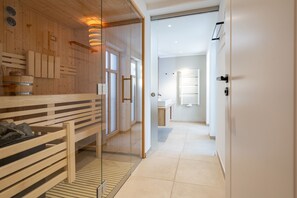 A modern hotel room with a wooden bench, a glass partition, and a bathroom with a sink and toilet.