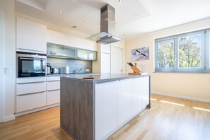 Et moderne køkken med en central ø, indbyggede hårde hvidevarer og et stort vindue.