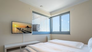 Une chambre à coucher avec un lit, un téléviseur fixé au mur, une fenêtre avec des stores et une vue sur la mer.