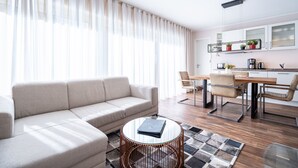 A modern living room with a sofa, a dining table with chairs, a coffee machine, and a kitchen area with cabinets and plants. - Quartier Ahlbeck, app. 04 (Heringsdorf)
