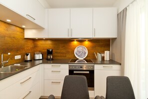 A compact kitchen with white cabinets, a stainless steel sink, a coffee maker, a toaster, and a dishwasher. There are two chairs in front of the counter. - Quartier Ahlbeck, app. 02 (Heringsdorf)