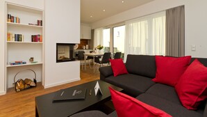 En moderne stue med sofa, reol og et spisebord i baggrunden.