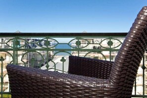 A wicker chair with a curved backrest, positioned on a balcony with a green metal railing.