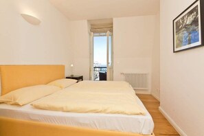 Une chambre à coucher avec un lit, une table de chevet, un radiateur et une vue sur l’extérieur, grâce à une porte ouverte.