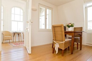 A room with a dining table, wicker chairs, a vase with flowers, and a view of the outside through a window.