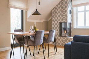 Un coin repas avec une table en bois et quatre chaises grises, un luminaire suspendu et un mur décoré situé derrière une cheminée.