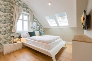 Une chambre avec un lit en mezzanine, une table de chevet, une lampe, une fenêtre avec des rideaux et un puits de lumière.