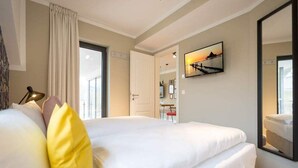 Quarto de hotel com uma cama grande, televisão fixada na parede e uma janela com cortinas.