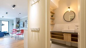 Um apartamento moderno com cozinha, área de refeições e banheiro com espelho redondo e prateleiras de madeira.