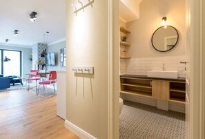 A modern apartment with a kitchen, dining area, and a bathroom with a round mirror and wooden shelves.