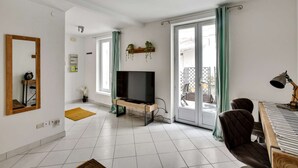 Un salon avec un téléviseur, un banc en bois, un piano et un balcon avec des rideaux.