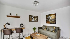 Un salon moderne avec un canapé gris, deux tabourets de bar, une table basse en bois, une œuvre d’art représentant un globe terrestre et une carte du monde accrochée au mur.