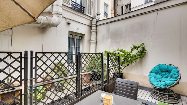 Une terrasse extérieure avec une table, des chaises, un fauteuil bleu rembourré et des plantes en pot.