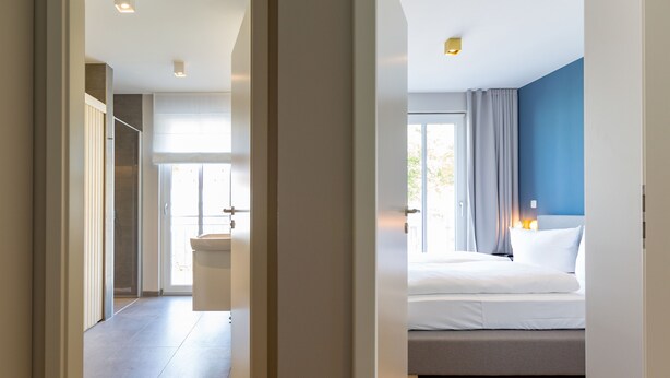 A modern hotel room with a large bed, a bedside table, and a window with curtains.