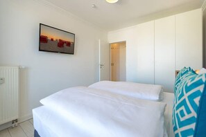Un dormitorio con dos camas, un radiador blanco, una puerta que da a un armario y un cuadro en la pared.