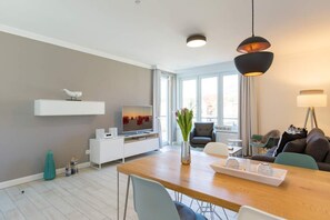Una sala moderna con una mesa de comedor de madera, un televisor de pantalla plana, un mueble blanco para la TV y un sofá.