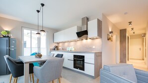 Una cucina moderna con mobili bianchi, forno integrato e illuminazione a sospensione.