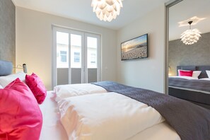 Quarto de hotel moderno com uma cama grande, vista para o mar pela janela e um quadro com uma cena de praia.