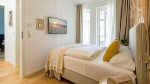 A bedroom with a bed, a painting, and a view of the outside. - Quartier am Kurpark, App. 12 Garden house (Heringsdorf)