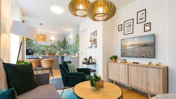 A modern living room with a sofa, chairs, a round coffee table, and a TV mounted on the wall. - Quartier am Kurpark, App. 12 Garden house (Heringsdorf)