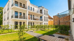 A multi-story residential building with balconies, a patio area with a table and chairs, and a well-maintained garden. - Quartier am Kurpark, App. 12 Garden house (Heringsdorf)
