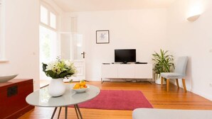 A modern living room with a glass table, a red rug, a white cabinet, a TV, and a plant. - Villa Astrid, T3 Münster (Heringsdorf)