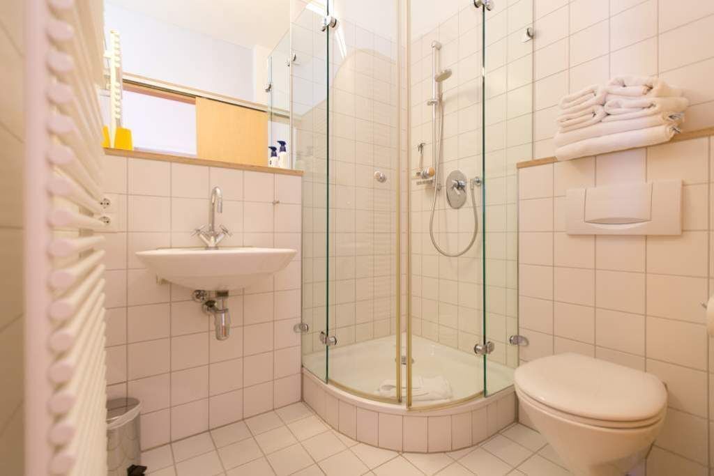 A corner bathroom with a glass-enclosed shower, a sink, and a toilet.