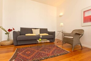 A living room with a grey sofa, a wicker chair, a patterned rug, a vase with flowers, and a lamp. - Villa Astrid, T4 Berlin (Heringsdorf)