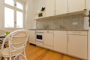 A kitchen with white cabinets, a microwave, an oven, and a dishwasher. There is a window with a view of buildings outside. - Villa Astrid, T4 Berlin (Heringsdorf)