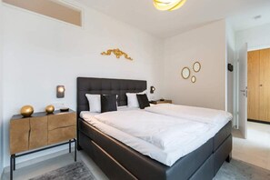 Quarto moderno com uma cama grande, mesa de cabeceira com abajur e arte decorativa na parede.