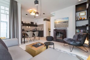Uma sala de estar moderna com um sofá, uma mesa de centro, lareira e uma área de jantar com cadeiras.
