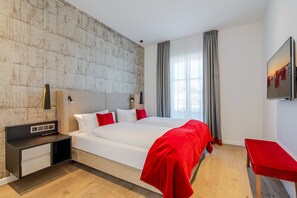 Une chambre d’hôtel moderne avec un grand lit, une table de chevet, une télévision et une vue sur la ville.