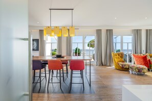 Un salon moderne avec un coin repas, de grandes fenêtres et une vue sur l’extérieur.