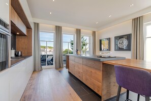 A modern kitchen with a wooden island, large windows, and a view of the outdoors. - Beachhouse Bansin, Penthouse Waterfront (Heringsdorf)