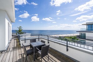 Un balcon avec vue sur la plage et l’océan, aménagé avec une table et des chaises.