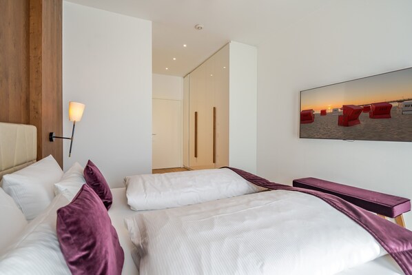 Ein Hotelzimmer mit zwei Betten, einem an der Wand befestigten Fernseher und einer Tür zu einem weiteren Raum.