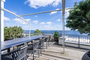 An outdoor deck with a long table and chairs, overlooking a beach and the sea. - Bansin Beach House, Waterfront Penthouse (Heringsdorf)