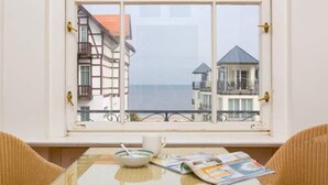 A room with a table by a window overlooking a coastal area with buildings and a view of the sea. - Villa Astrid, T1 Cologne (Heringsdorf)