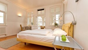 A bedroom with a bed, bedside table, lamp, and a window with curtains. - Villa Astrid, T1 Cologne (Heringsdorf)