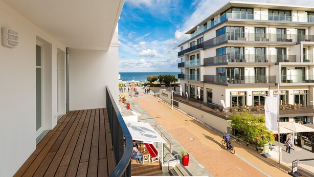A balcony with a wooden floor, overlooking a beachside promenade with buildings and shops. - Beachhouse Bansin, app. 14 (Heringsdorf)