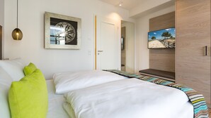 A modern bedroom with a large bed, a wall-mounted TV, and a framed artwork. - Beachhouse Bansin, app. 14 (Heringsdorf)