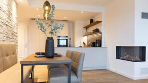 Een moderne woonkamer met een bank, een eettafel met stoelen, een open haard en een keuken met een fornuis en kasten.