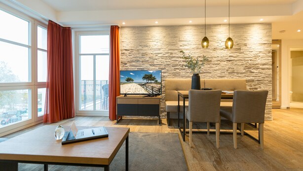 Een moderne woonkamer met een stenen accentmuur, een bank, een eettafel met stoelen en een groot raam met gordijnen.