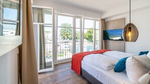 Ein Schlafzimmer mit großem Fenster, einem Bett mit weißer Bettwäsche und einer roten Decke.