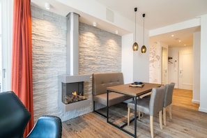 A modern living room with a stone wall, a fireplace, a dining table with chairs, and a red curtain. - Beachhouse Bansin, App. 21 (Heringsdorf)